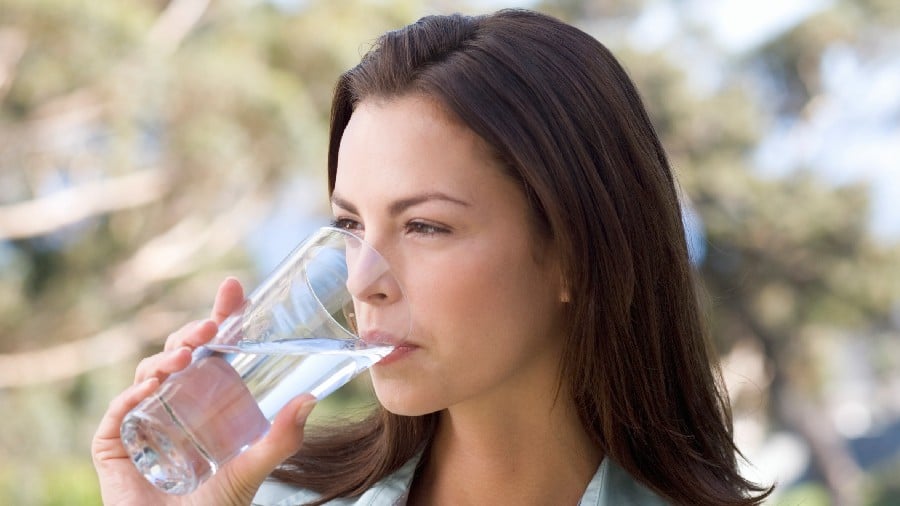 אישה שותה מים כדי למנוע יובש בפה